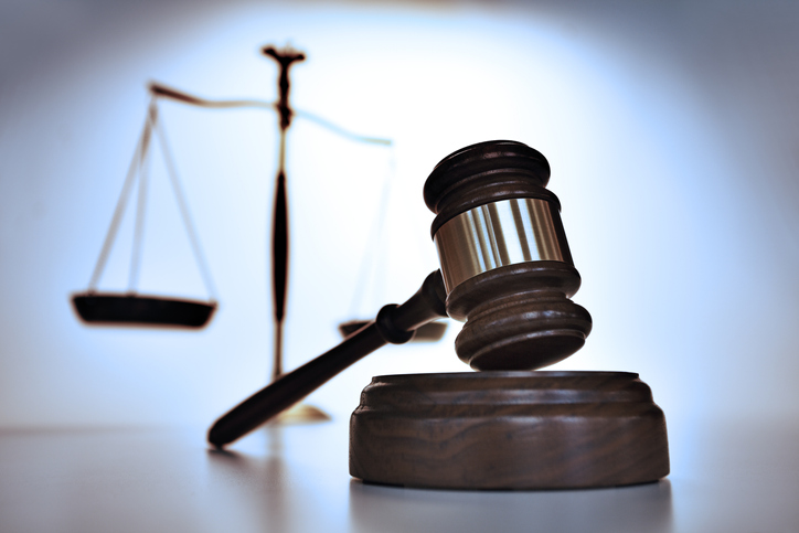 A close up of a gavel with a justice scale out of focus in the background. Photographed with a very shallow depth of field.