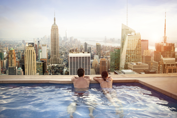 Couple relaxing in swimming pool on hotel rooftop, overlooking impressive New York skyline.