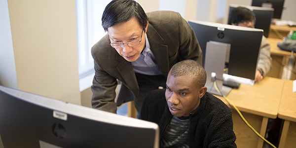 student in front of computer with professor standing behind him