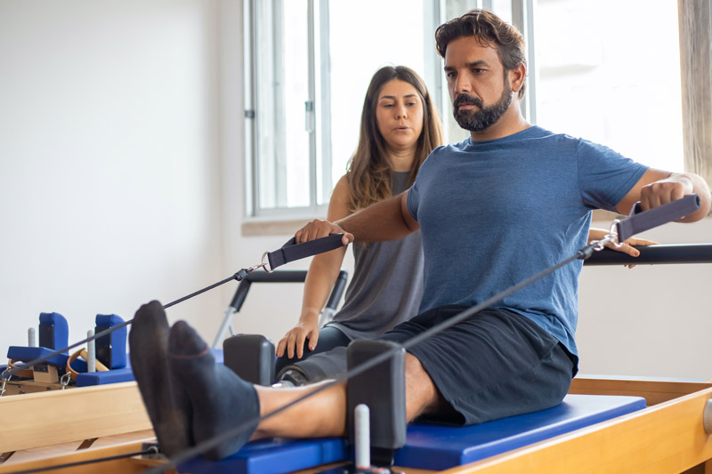 female physical therapy assistant standing behind man receiving assistance