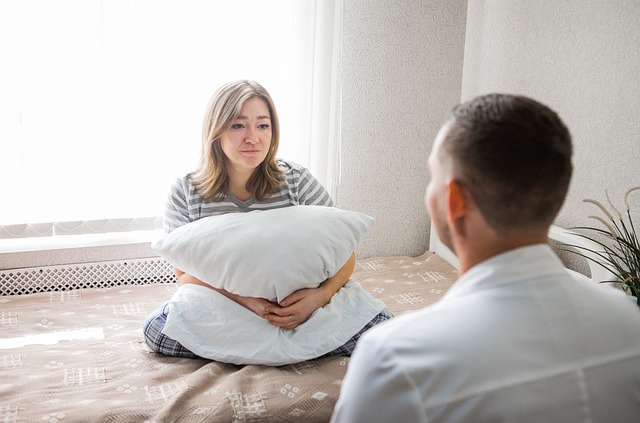 woman on bed holding pillow, facing man