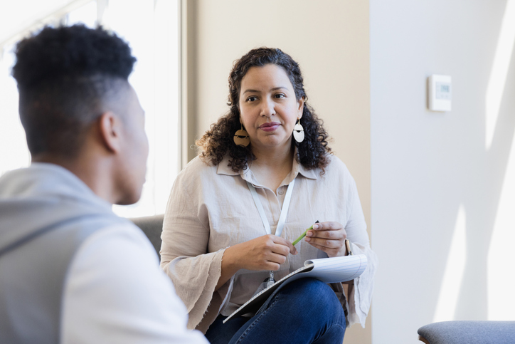 The counselor listens to the young adult and takes notes for their next meeting.