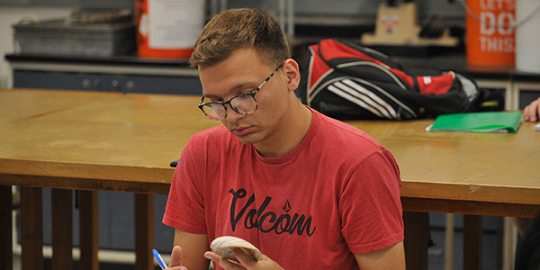 student in red shirt looking at shell